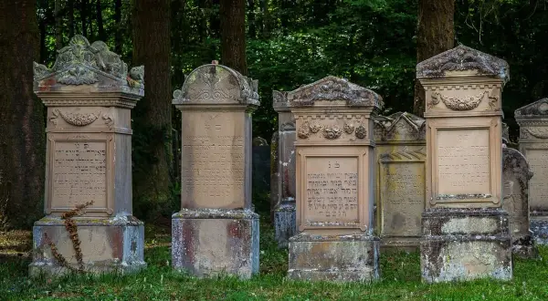 Nagrobki z inskrypcjami hebrajskimi, niektóre z widocznymi pęknięciami, sugerującymi wady materiałowe płyt granitowych.