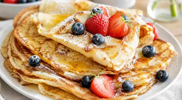 Ein Stapel goldbrauner Pfannkuchen, bestäubt mit Puderzucker und garniert mit frischen Beeren und Honig. Ein einfaches Pfannkuchen-Rezept, das jeden Tag zum Genuss macht.