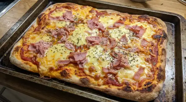 En nygräddad pizza med rikligt med smält mozzarella och skinka, redo att avnjutas.