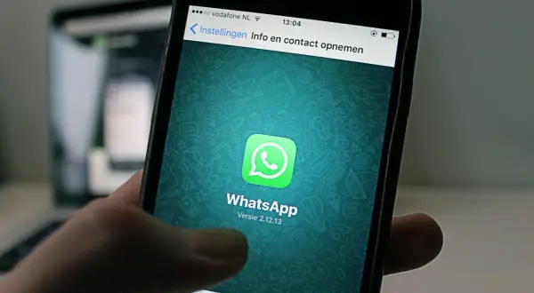 Dłoń trzyma smartfon z otwartą aplikacją **WhatsApp Business**. Na ekranie widnieje zielone logo aplikacji i jej nazwa.