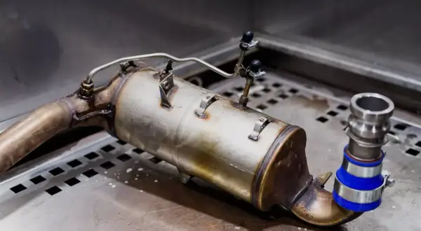 Element układu wydechowego, prawdopodobnie zapchany DPF, z widocznymi przewodami i złączkami. Objawy zapchanego dpf mogą być różne.