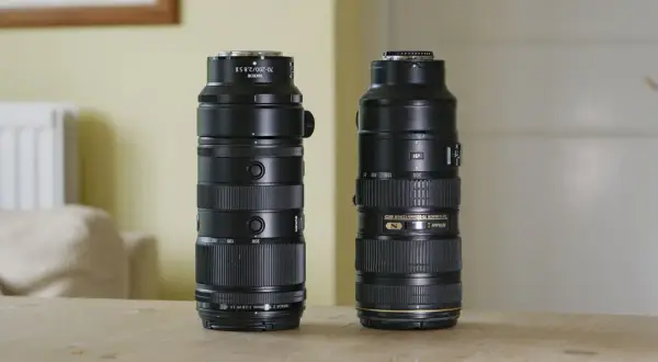 Two Nikon telephoto lenses, including a Nikkor 200mm f2, stand side-by-side on a wooden table.