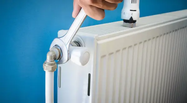 Réparation d'un radiateur bruyant. Une clé serre un raccord, peut-être pour arrêter l'eau qui coule.