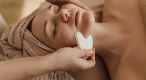 Un viso rilassato riceve un massaggio con pietra gua sha, una tecnica che serve a migliorare la circolazione e il drenaggio linfatico, donando luminosità.