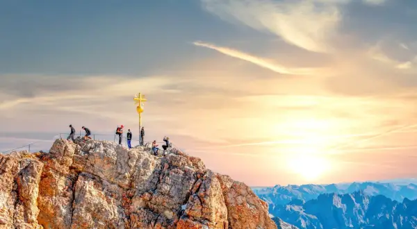 Menschen auf dem Gipfel der Zugspitze mit goldenem Kreuz. Die Zugspitze Aufstieg Dauer ist lang, aber die Aussicht ist es wert.