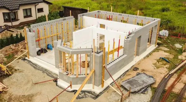 Budowa domu energooszczędnego z bloczków betonowych i białych płyt izolacyjnych. Widać zbrojenia i elementy konstrukcyjne.