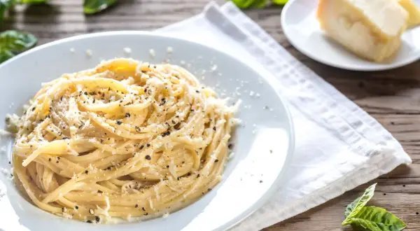 Un piatto di spaghetti fumanti conditi con abbondante cacio e pepe, guarniti con pecorino grattugiato e pepe nero macinato fresco.
