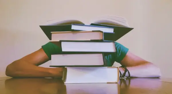 Stos książek przygniata głowę studenta. Jak napisać dyskusję w pracy magisterskiej? Czas na naukę!