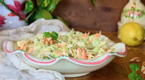 Deliciosa ensalada de col cremosa con zanahoria rallada, coronada con nueces y perejil. Perfecta para acompañar cualquier comida.