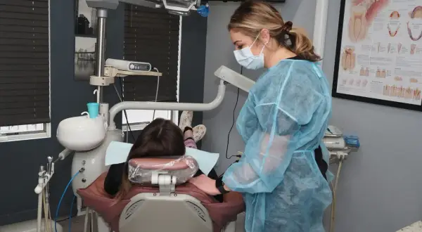 Dentystka w fartuchu przygotowuje się do skalingu i piaskowania NFZ. Pacjentka leży w fotelu.