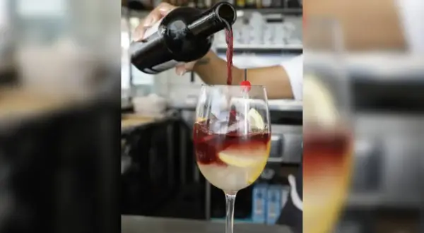 Rotwein wird in ein Glas mit Eis, Zitrone und Kirsche gegossen. Perfekt für rotwein im sommer.