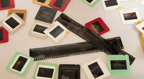 Stare klisze filmowe i slajdy, niektóre w kolorowych ramkach. Widać fragmenty negatywów z perforacją.