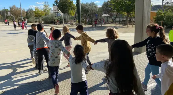 Niños jugando en círculo, tomados de la mano, en una actividad de juegos de conocimiento del medio al aire libre.