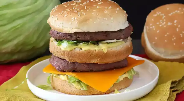 Burger double étage avec fromage, laitue et sauce sur une assiette blanche.