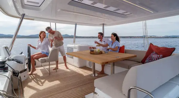 Coppia felice brinda a bordo di un catamarano, godendosi il sole e il mare. Interni eleganti e confortevoli.