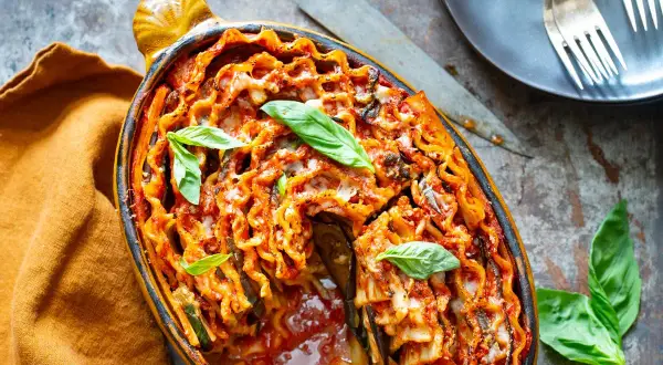 Lasagne aubergine gratinée, garnie de basilic frais, dans un plat ovale. Un délice italien réconfortant.