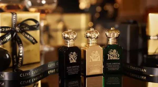 Trzy butelki najdroższych perfum Clive Christian w złotych opakowaniach, ozdobione czarną wstążką z logo marki.