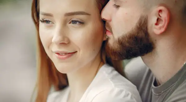 Un uomo sussurra dolcemente all'orecchio di una donna, un gesto che rivela cosa fa innamorare un uomo: la tenerezza e l'intimità.