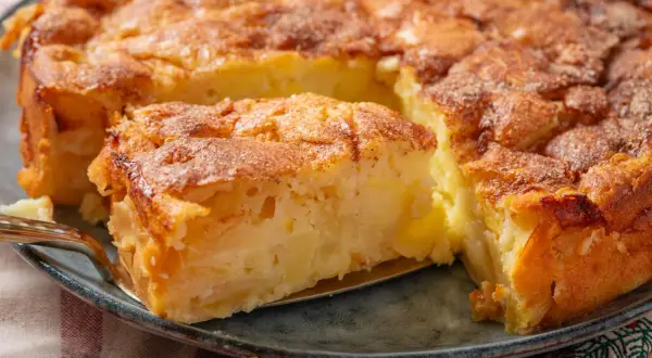 Ein goldbrauner Apfelkuchen, der nach einem einfachen Apfelkuchen Rezept duftet. Ein Stück wird mit einer Gabel herausgehoben.