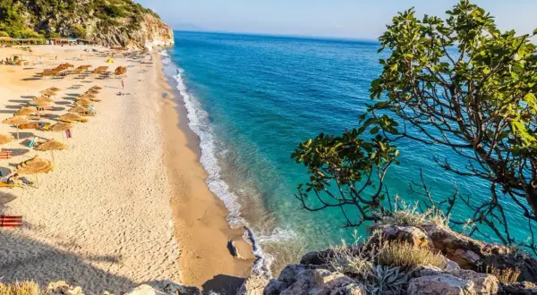 Piękna plaża w Albanii z turkusową wodą i rzędami parasoli. Ceny wakacji w Albanii są przystępne, a widoki zachwycające.