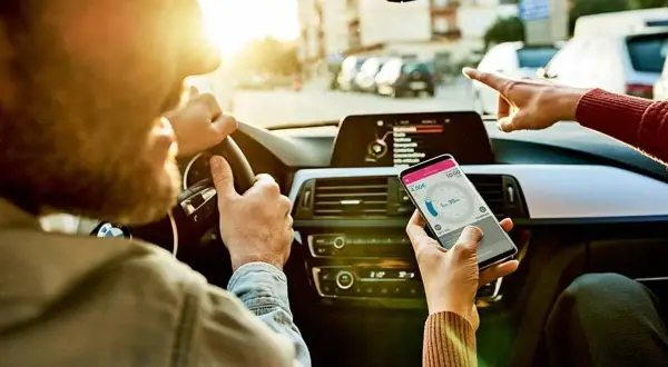 Kierowca i pasażerka sprawdzają nawigację w telefonie, ustalając trasę i czas podróży.