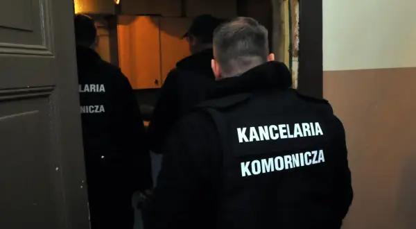 Osoby w kamizelkach z napisem "KANCELARIA KOMORNICZA" wchodzą do pomieszczenia. Może to być związane ze skargą na czynności komornika.