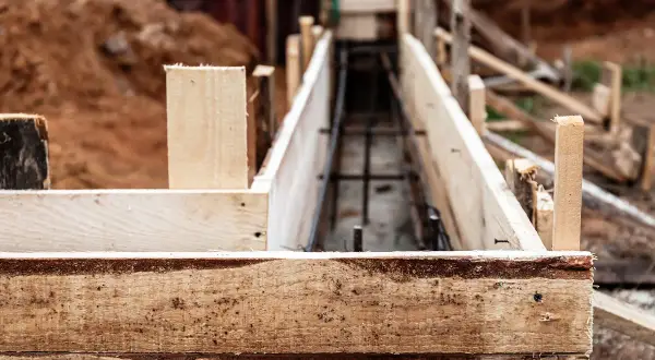 Drewniana szalunkowa konstrukcja przygotowana pod fundament pod ogrodzenie. W środku widoczna zbrojenie.
