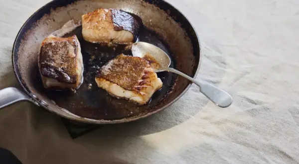 Stekt kolja i en panna, perfekt för ett enkelt kolja recept. En sked ligger bredvid fisken.
