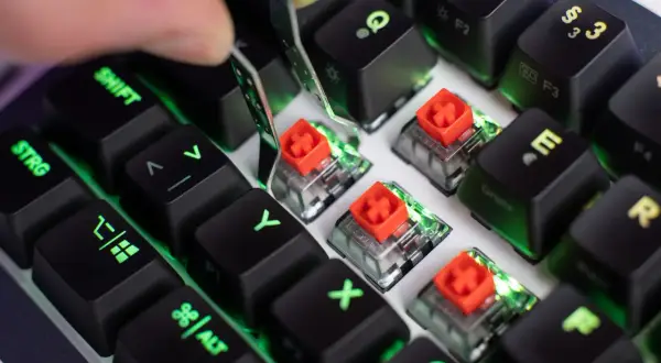 Nahaufnahme von Tastatur-Switches mit roten Kappen, die Unterschiede zeigen. Grüne Beleuchtung schimmert durch.