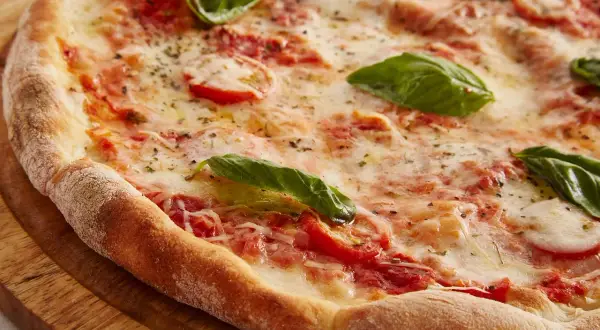 Zbliżenie na świeżo upieczoną pizzę z pomidorami, mozzarellą i bazylią na drewnianej desce.