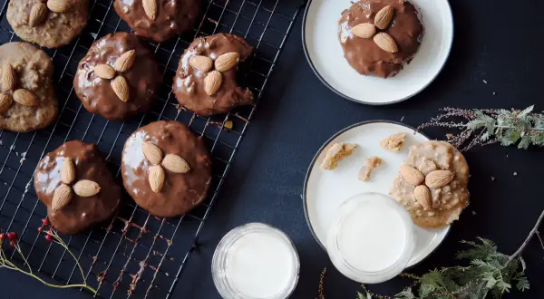 Schokoladenüberzogene Elisenlebkuchen mit Marzipan und Mandeln auf einem Gitter, daneben Milchgläser und Tannenzweige.