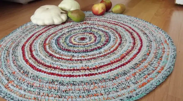Tappeto uncinetto rotondo con fantasie a spirale multicolore. Sopra, zucche bianche, una pera e mele rosse.