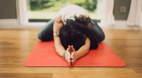 Mujer en postura de niño en esterilla roja, practicando una de las 20 posturas de yin yoga.