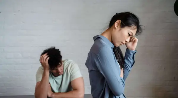 Pareja con intermitencia emocional, ella con la mano en la frente, él con la cabeza entre las manos, ambos de espaldas.