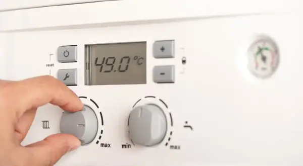Dłoń reguluje pokrętłem pieca gazowego. Na wyświetlaczu 49°C. Jaka temperatura na piecu gazowym dla ogrzewania podłogowego?