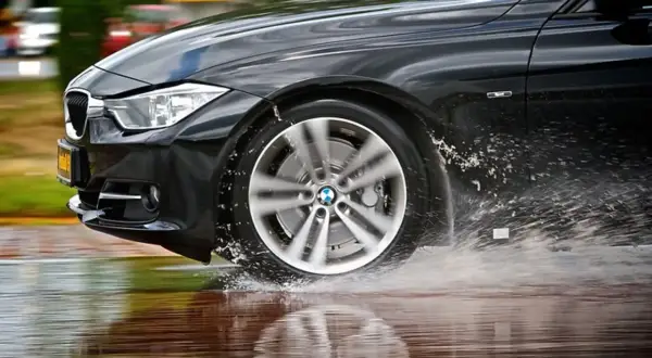 Schwarzer BMW fährt durch Wasserpfützen, was auf einen Uniroyal RainSport 5 Test hindeutet.