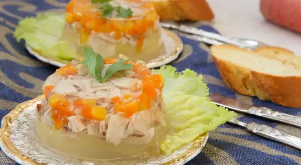 Elegancka ryba w galarecie z marchewką i natką pietruszki, podana na liściu sałaty z pieczywem.