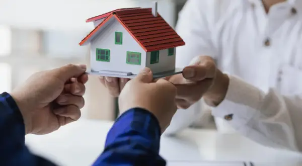 Manos intercambian una maqueta de casa, simbolizando la decisión de vender herencia.