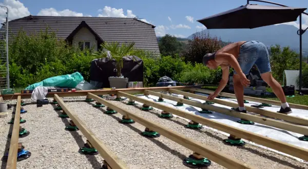 Mann baut einen Holzpodest auf Stelzlagern. Das Fundament für die Terrasse wird vorbereitet.