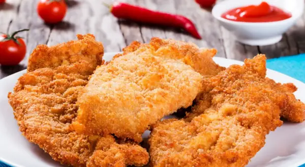 Chrupiące sznycle na białym talerzu, obok pomidorki i papryczka chili. Idealne na obiad!
