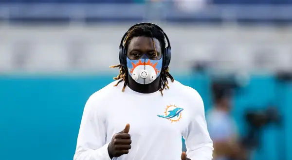 Miami Dolphins player running with an altitude mask training, headphones on, and giving a thumbs up.