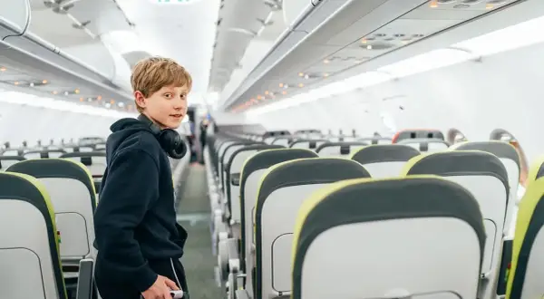 Chłopiec z słuchawkami na szyi w pustym samolocie. Zastanawia się, od ilu lat można latać samemu Ryanair.