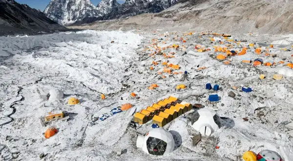 Zahlreiche bunte Zelte auf schneebedecktem Geröllfeld am Fuße des Mount Everest. Ein Basislager, das die Herausforderungen des Gipfels widerspiegelt.