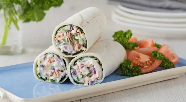 Trois wraps au thon crémeux, garnis de thon, oignons rouges et concombre, servis avec des quartiers de tomates et du persil.