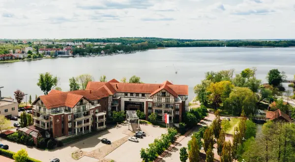 Willa Port w Ostródzie, hotel z widokiem na jezioro, otoczony zielenią i zabudowaniami.