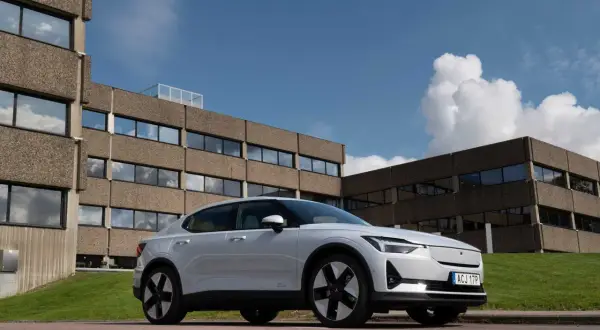Vit Polestar 2 parkerad framför ett modernistiskt betonghus. Bilen är redo för en polestar 2 testkörning i solsken.