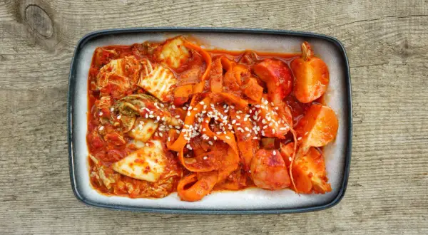 Gotowe kimchi z kapusty pekińskiej, z marchewką i sezamem, na drewnianym tle. Idealne do nauki jak zrobić kimchi z kapusty pekińskiej.