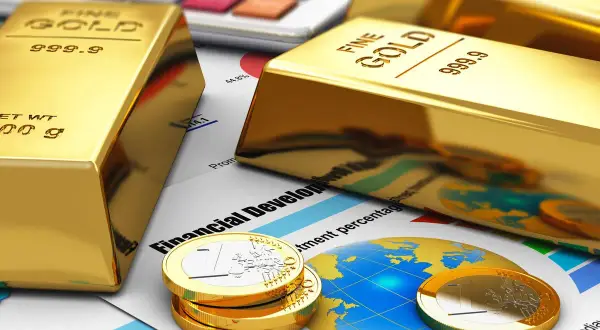 Sztabki złota i monety euro na tle wykresów i kalkulatora symbolizują inwestycję w złoto jako bezpieczną przystań finansową.