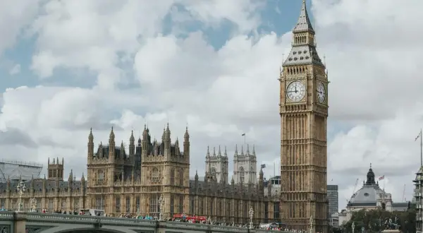 Big Ben i Parlament w Londynie, stolicy UK, na tle chmur. Most pełen ludzi i czerwony autobus.