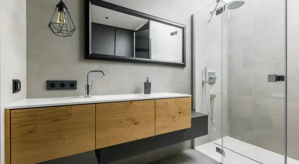 Meuble de salle de bain en bois avec une belle profondeur, miroir, robinetterie moderne et douche vitrée.